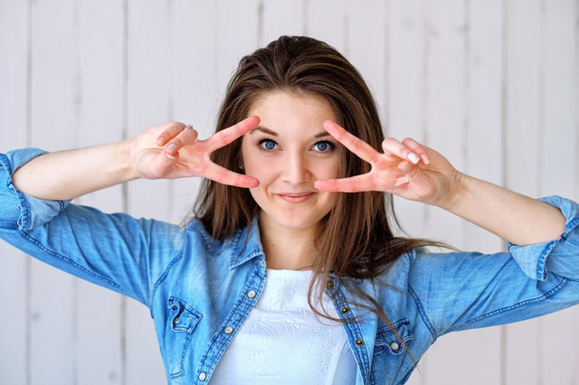 Female in jean jacket smiling and giving peace sign