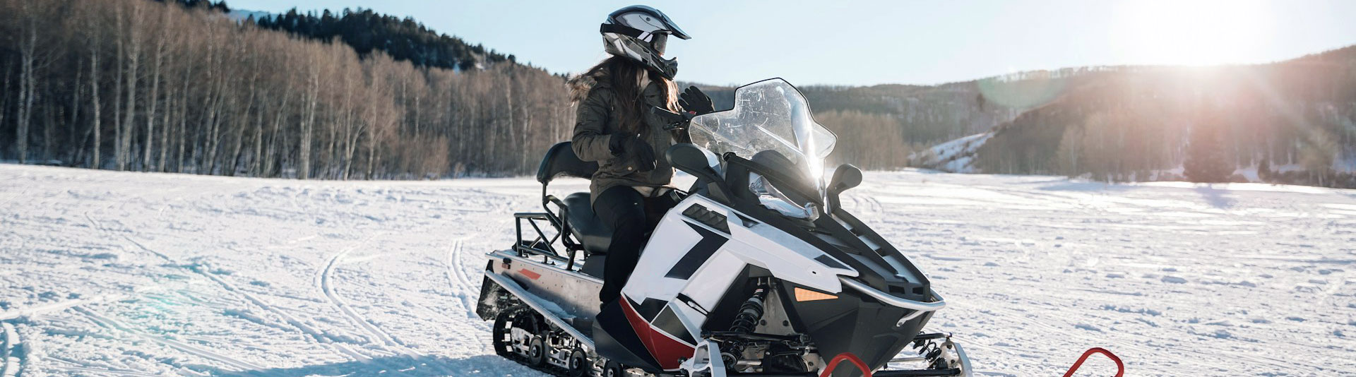 Female riding a snowmobile through a winter forest on a sunny day