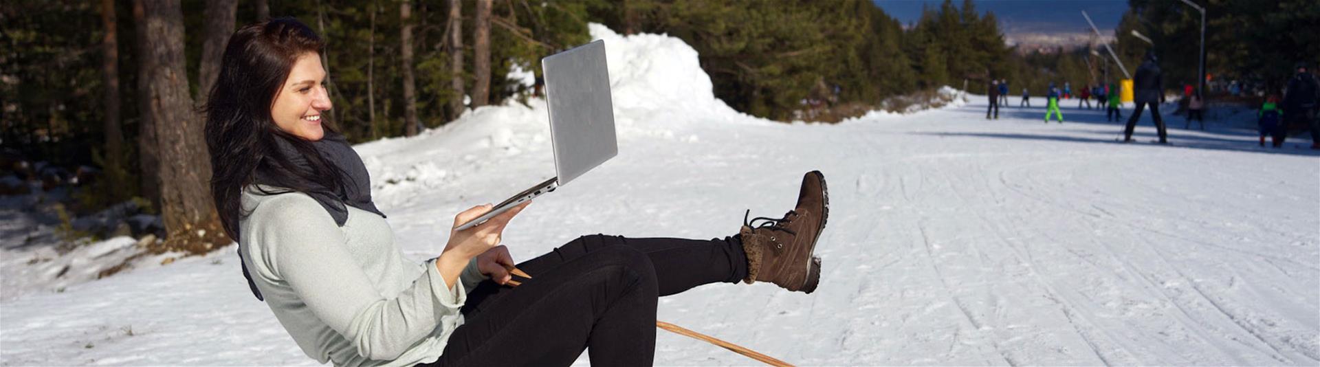 Happy female sitting on sled using a laptop