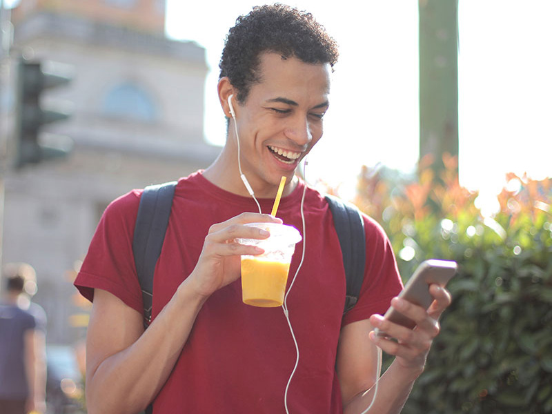 Happy Male outside drinking a smoothie on his phone smiling