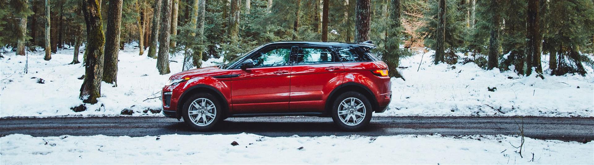 Red car driving down forest road during Winter