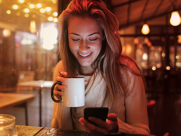 Woman in sweater Holding Mug happily Looking at Her Cellphone