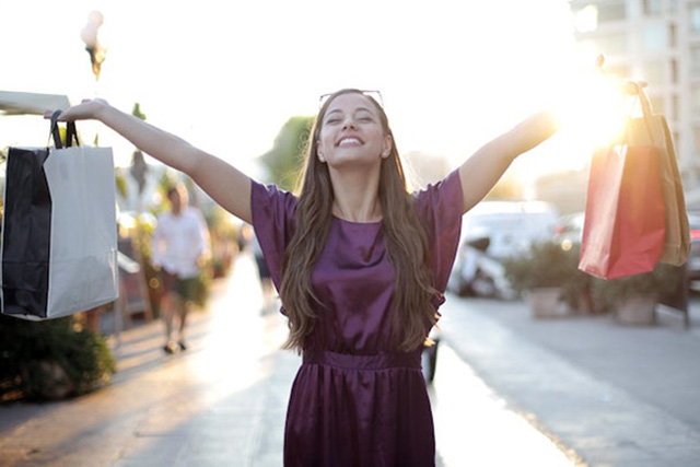 female outside in purple dress holding her shopping bags up and smiling