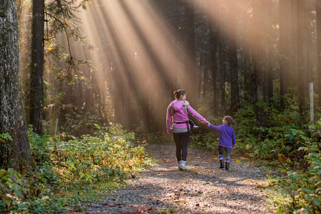 Mother walking with her daughter down a hiking trail with sun rays beaming through trees